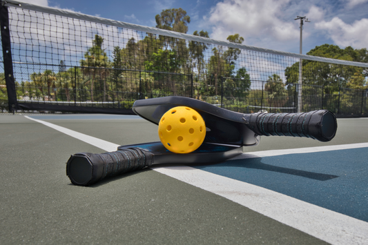 Two pickleball paddles and a yellow ball on the court