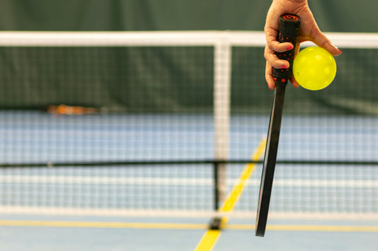 A person holding a pickleball and paddle.